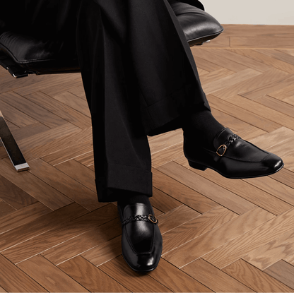 Mocassini in pelle nera slip-on 1500F3R00F100 indossati, design elegante con fascia intrecciata su pavimento in legno.